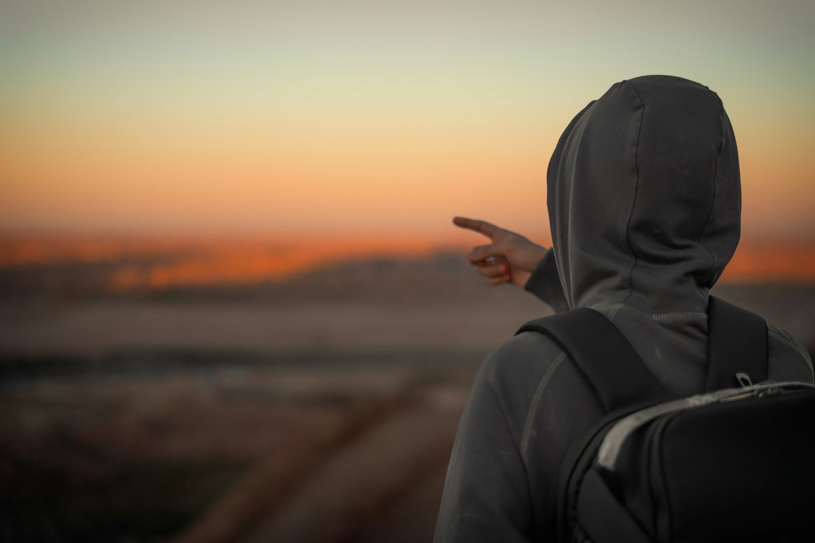 A young person with a backpack looking out toward the horizon at sunset